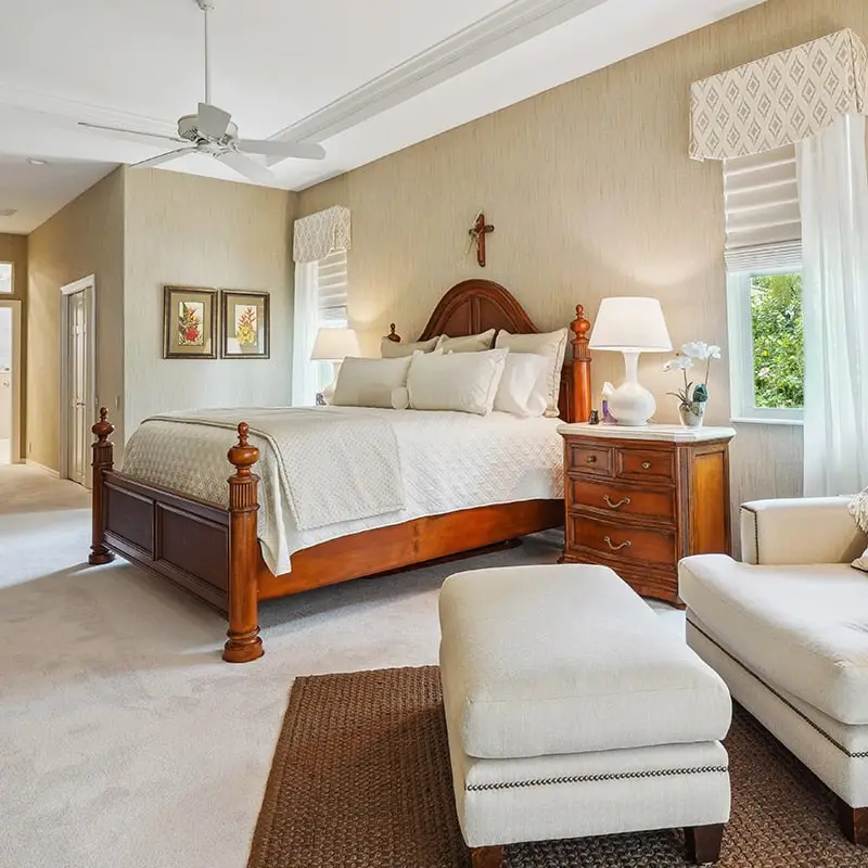 Bright and inviting bedroom with large wooden bed, cream bedding, and soft lighting. Elegant decor including framed art and floral accents creates a tranquil sleep space.