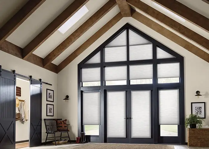 Beautiful interior featuring large black-framed barn doors with white shades, vaulted ceiling with wooden beams, cozy seating area, and decorative artwork.