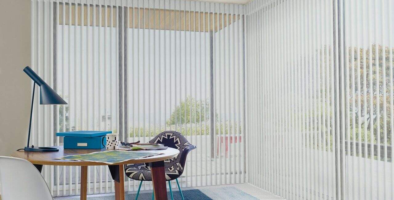 Modern workspace with vertical blinds, desk lamp, and colorful chair offering a relaxing and functional office area, perfect for working or reading.