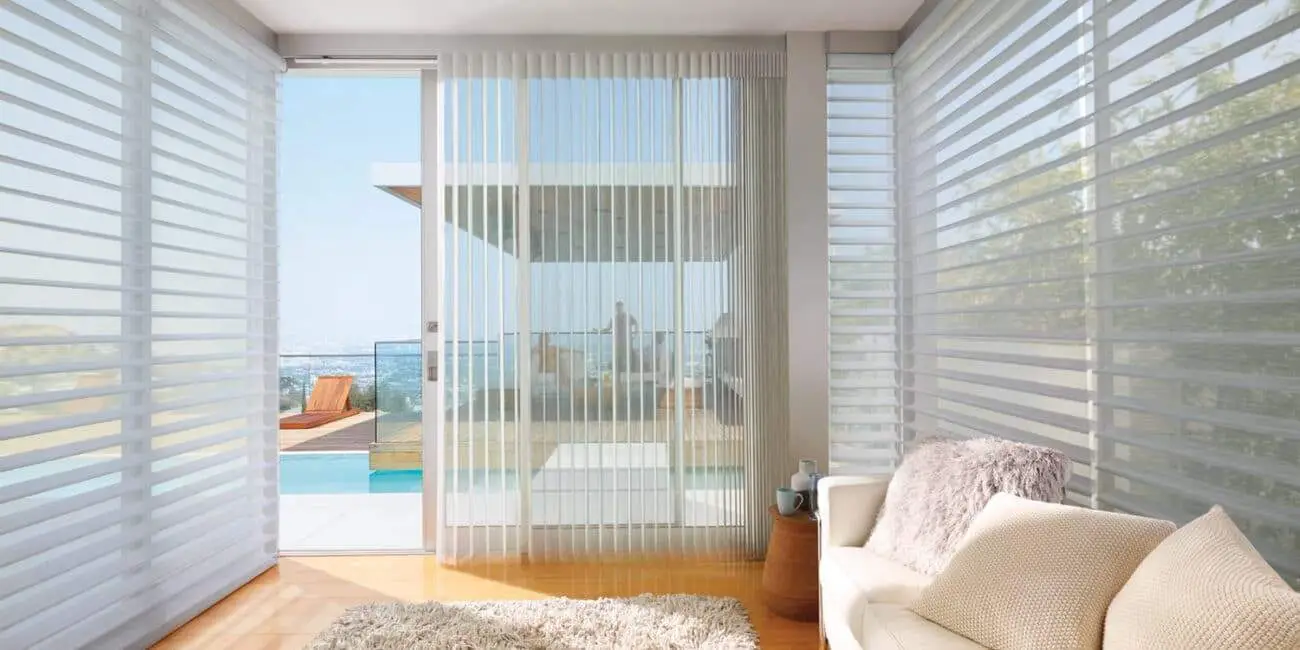 Bright, airy living space featuring expansive windows, vertical blinds, cozy sofa, and a view of the balcony and outdoor pool area.