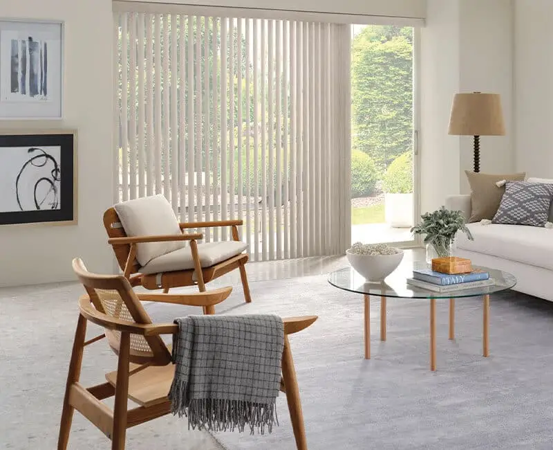 Bright and airy living room with minimalist decor, large window with vertical blinds, cozy seating with wooden chairs and a neutral color palette, perfect for relaxation and entertaining.