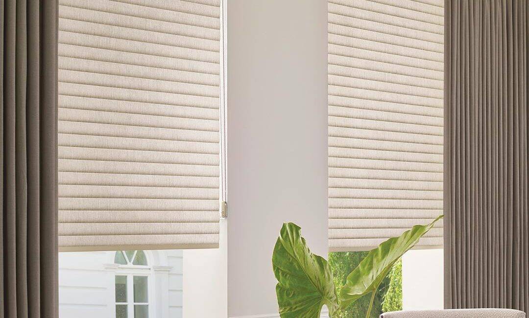 High-quality beige and dark gray window blinds with matching curtains, allowing natural light to flow into a cozy, stylish space with decorative plant and books.