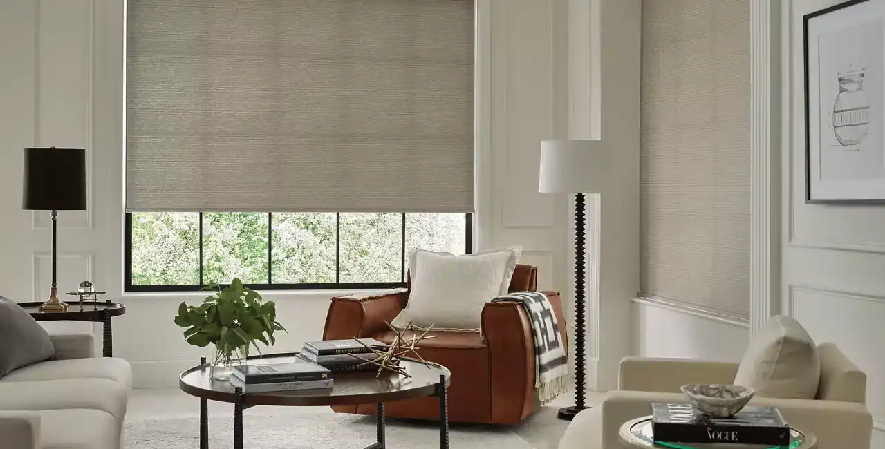 Bright and inviting living room with large windows, beige blinds, and elegant furniture including white sofas, a leather armchair, and stylish side tables.