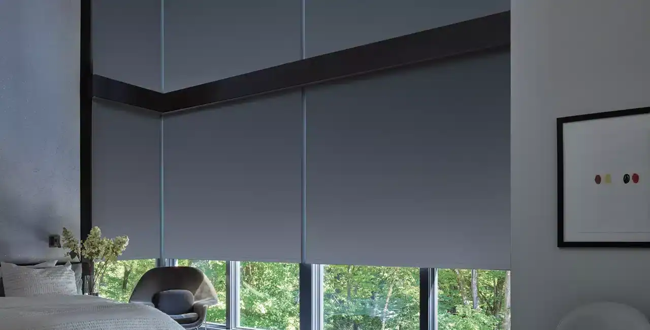 Luxurious bedroom featuring floor-to-ceiling windows with gray roller shades, contemporary furniture, and a serene natural backdrop.