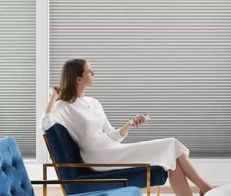 Woman relaxing in sleek office lounge, sitting on stylish blue velvet armchair, using smartphone, natural light from big windows, minimalist decor, professional environment.
