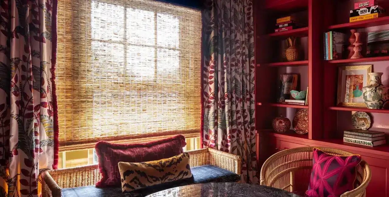 Bright window with bamboo blinds, floral curtains, and colorful cushions create a warm, inviting space for reading or relaxing.