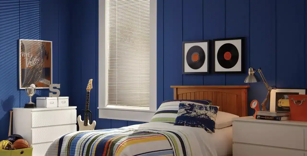 Bright blue bedroom wall with vinyl record art, a white dresser, skateboard, and sports gear, creating a vibrant and lively ambiance. Natural light filters through blinds, illuminating the colorful bedrooms' decor perfect for a creative personality.