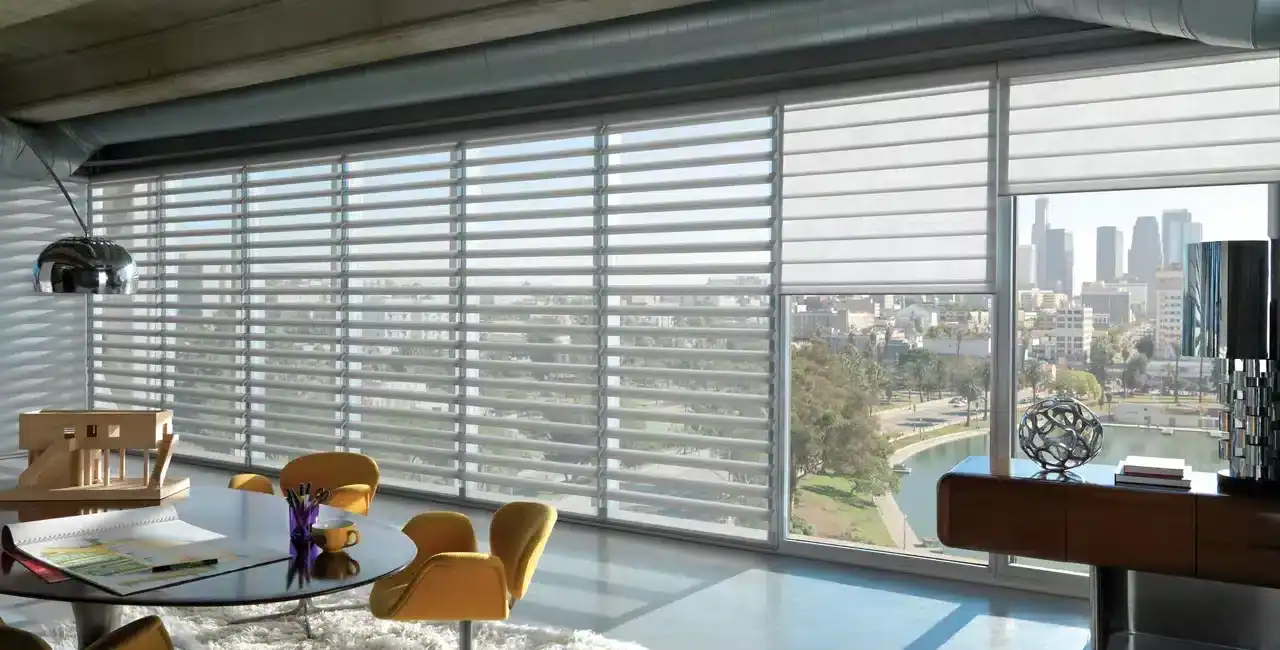 Modern office space with large windows and adjustable blinds overlooking a city skyline and park, bright natural lighting, stylish furniture, and contemporary decor.