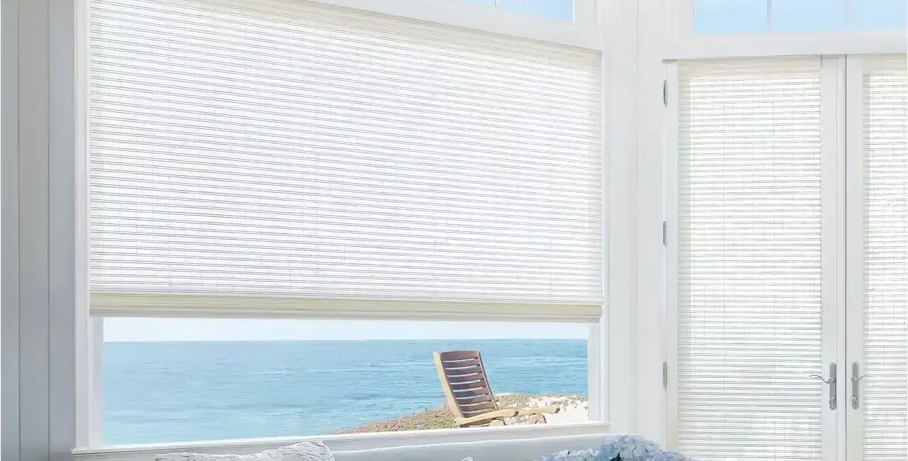 Bright ocean view through white window blinds with beach scenery outside.
