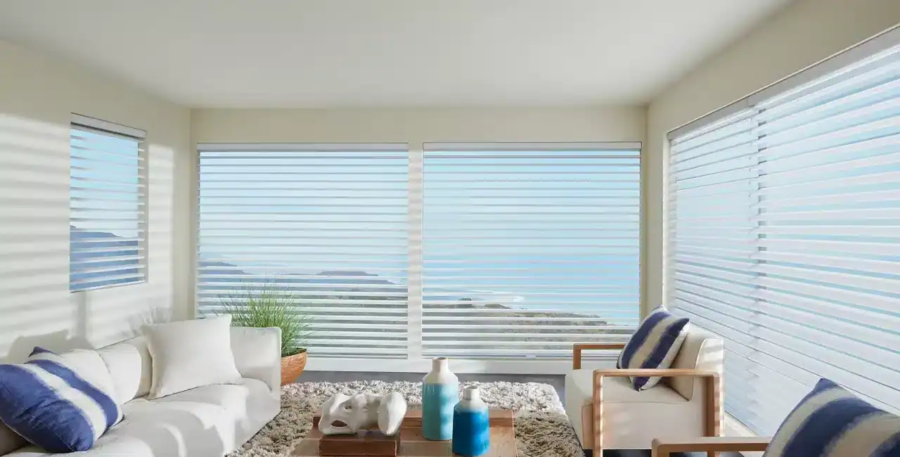 Bright living room with panoramic ocean view, white furniture, and horizontal blinds.