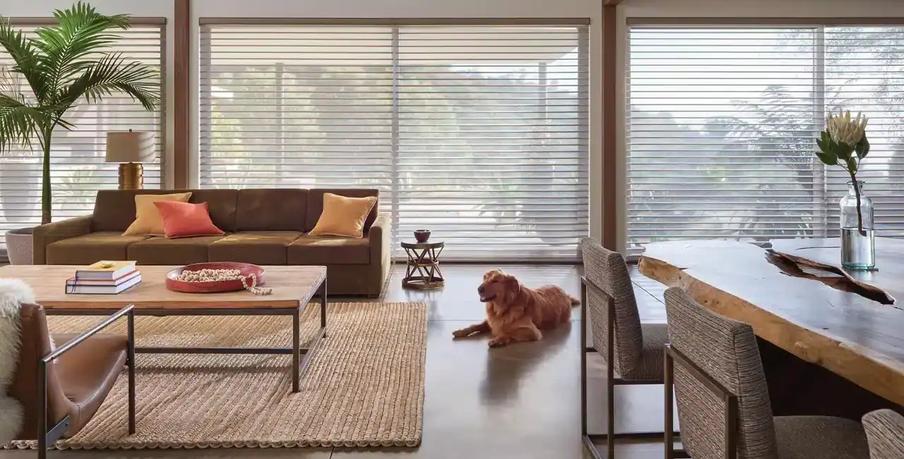 Bright living room with large windows, stylish furniture, a dog lying on a hardwood floor, lush plants, and decorative accents, creating a warm and inviting atmosphere.