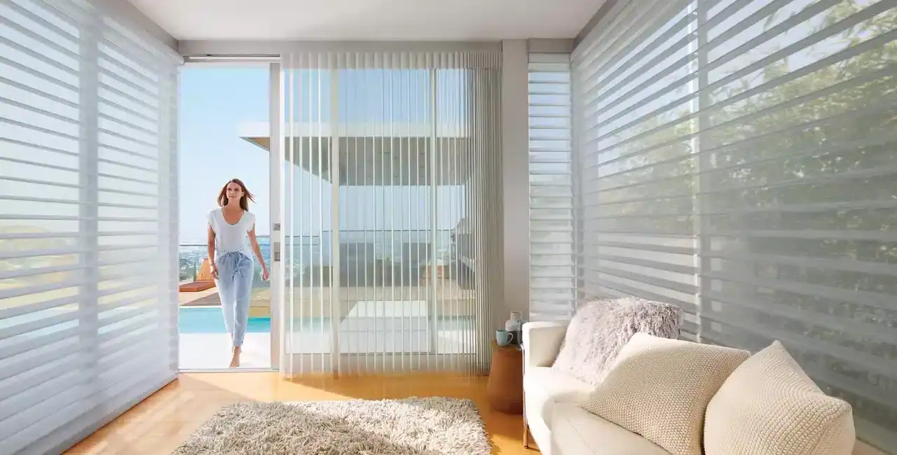 Sunroom with large glass sliding doors, vertical blinds, and cozy beige sofa, offering a bright, airy space with natural light and scenic outdoor views.