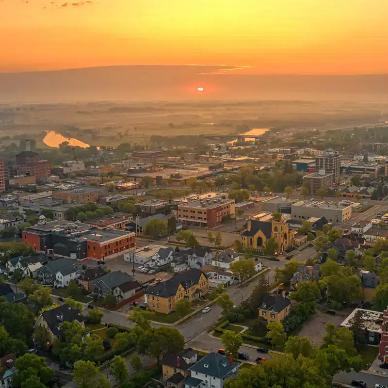 Aerial view of an urban area during sunset, showcasing a mix of houses, streets, and city infrastructure with a vibrant sky.