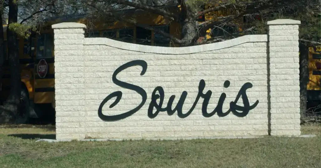 Welcome sign in Souris, Manitoba, featuring the town's name on a white brick wall with a scenic background.